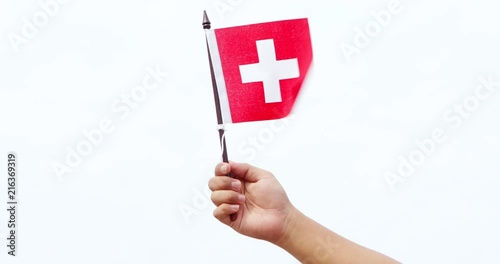 Human hand holding Switzerland national flag under clear sky with white clouds. Shot outdoors in 4k resolution photo