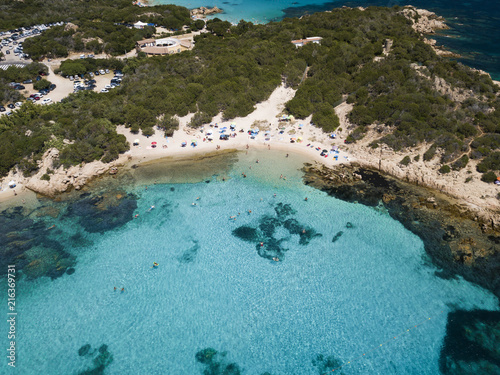 View from above, aerial view of an emerald and transparent Mediterranean sea with a white beach full of colored beach umbrellas and tourists who relax and swim. Costa Smeralda, Sardinia, Italy.