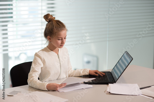 young girl businesswoman in casual clothes  sitting at a table closely look at documents  working at computer