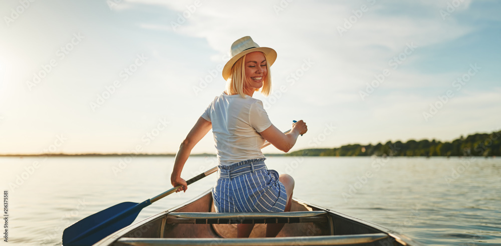 Smiling woman canoeing on a still lake in the summer - obrazy, fototapety, plakaty 