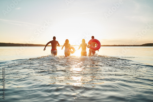 Friends running into a lake at sunset splashing water