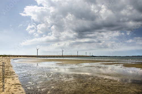 Clouds over the dam in Haringvliet estuary reflecting in shallow lakes on the beach near Rockanje, The Netherlands photo