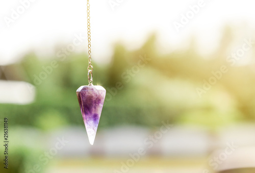 Purple Amethyst crystal pendulum on chain, outdoors trees and nature on the background. photo