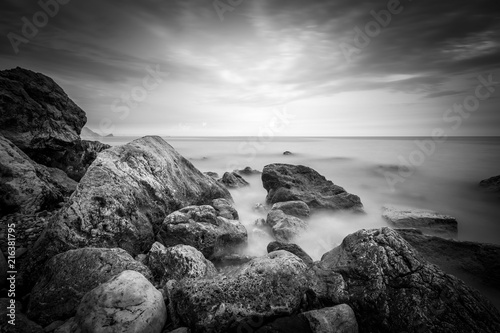 Sea coast with rocks and stones on long exposure. Dramatic black and white seascape.