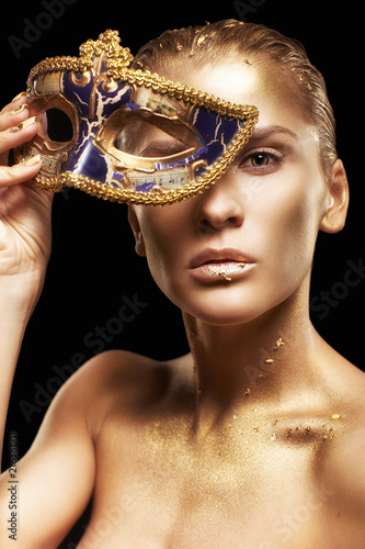 Female with masquerade venecian mask in hand near face. Golden girl on black background