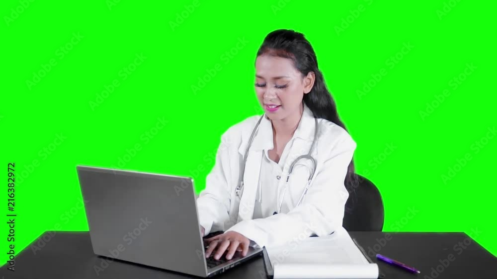 Slow motion of beautiful female doctor working with a laptop computer on the table and smiling at the camera with green screen background Slow motion of beautiful female doctor working with a laptop computer on the table and smiling at the camera with green screen background