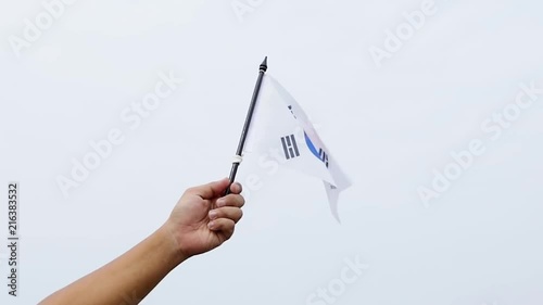 Slow motion of human hand waving South Korean national flag under clear sky with white clouds photo