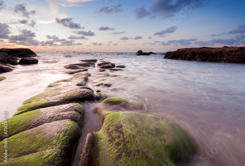 view of beautiful sunset at the beach with natural coastal rocks covered by green moss. soft focus due to slow shutter effect.