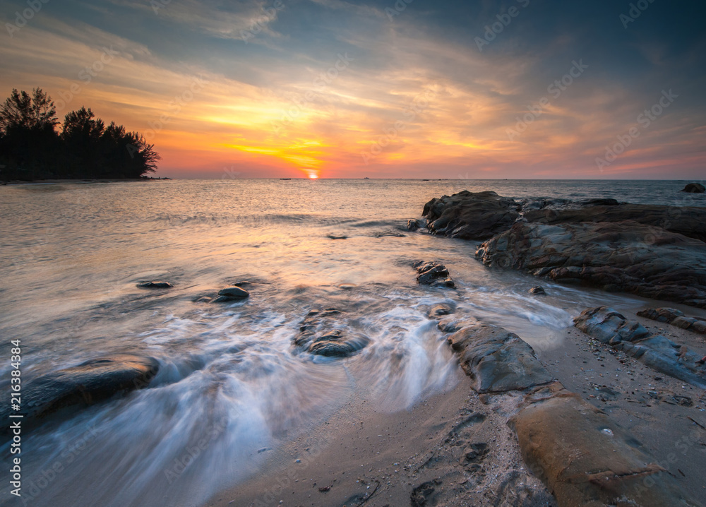 Obraz premium view of beautiful sunset at the beach with natural coastal rocks covered by green moss. soft focus due to slow shutter effect.