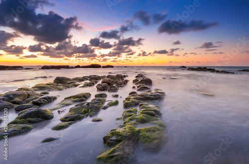 view of beautiful sunset at the beach with natural coastal rocks covered by green moss. soft focus due to slow shutter effect. © udoikel09