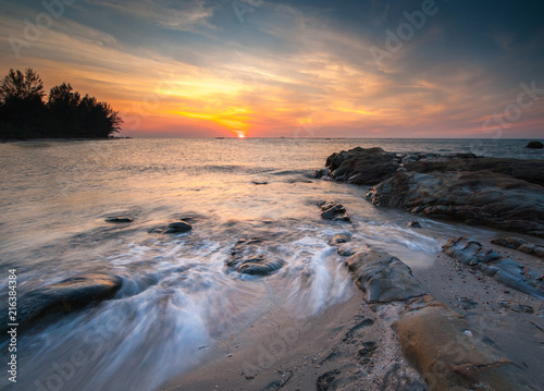 view of beautiful sunset at the beach with natural coastal rocks covered by green moss. soft focus due to slow shutter effect.