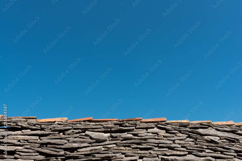 Old roof with grey stone tiles and clear blue sky in background Old roof with grey stone tiles and clear blue sky in background