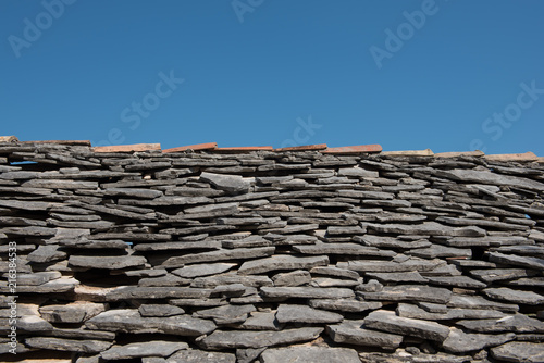 Old roof with grey stone tiles and clear blue sky in background