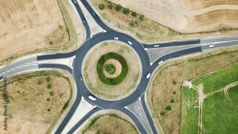 Roundabout aerial overview footage from above with vehicles circling around the traffic circle lane, France country side rural road transportation top view, summer day, cars and trucks