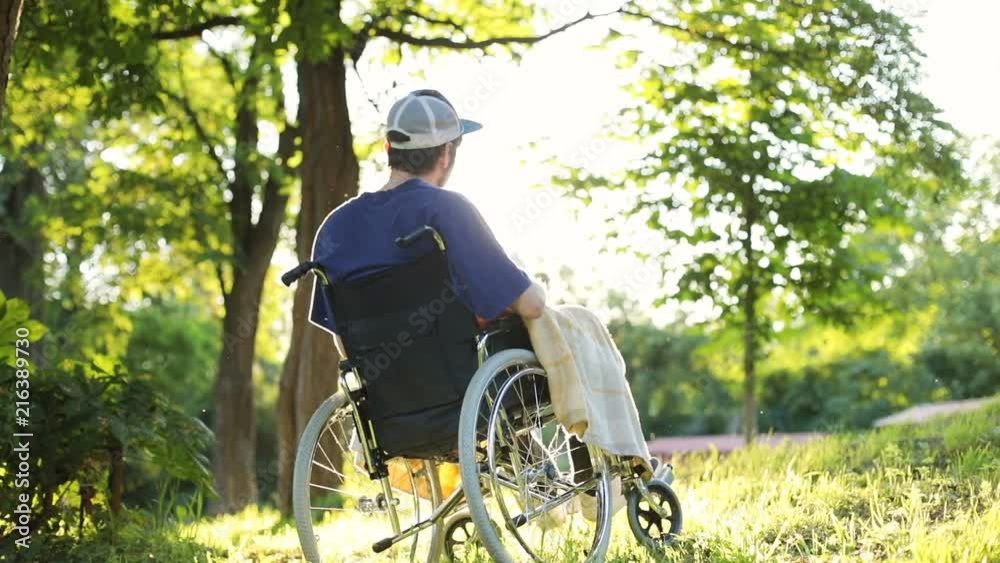 back view of young man resting outside sitting on wheelchair with beautiful bright sunshine rises on background enjoying green nature healthcare concept responsibility rehabilitation therapy back view of young man resting outside sitting on wheelchair with beautiful bright sunshine rises on background enjoying green nature healthcare concept responsibility rehabilitation therapy