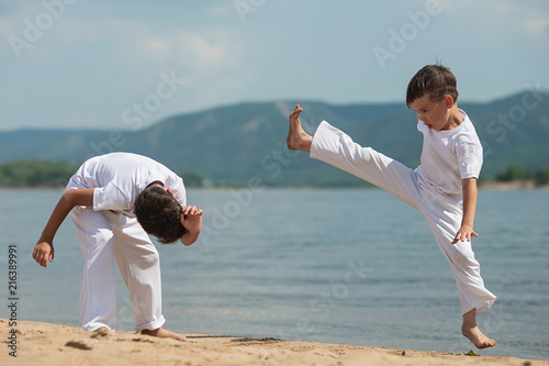 Training of two children on the beach: capoeira, sports