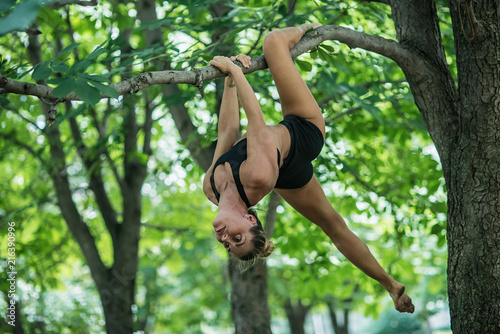 Girl acrobat performs acrobatic element on the tree. Woman engaged in gymnastics