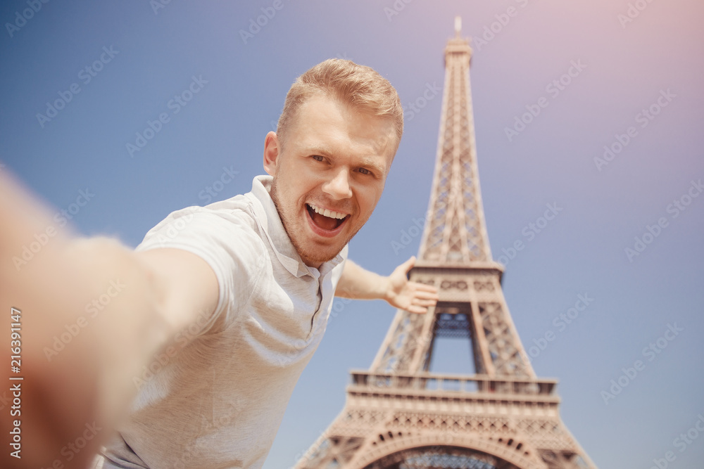 Happy man tourist is making photograph of Selfie on background of Eiffel Tower in Paris, France. Concept travel, rest.