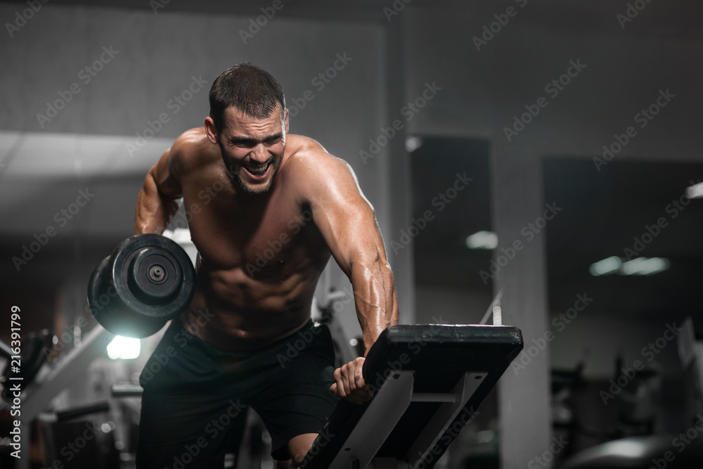 Man trains in the gym. Athletic man trains with dumbbells, pumping his biceps Man trains in the gym. Athletic man trains with dumbbells, pumping his biceps