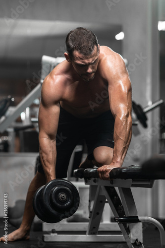 Man trains in the gym. Athletic man trains with dumbbells, pumping his biceps