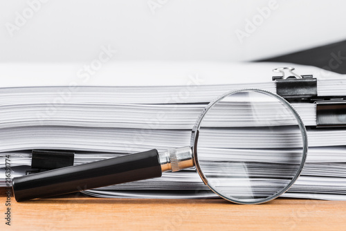 Close-up magnifying glass place on wooden table and search to edge of white documents