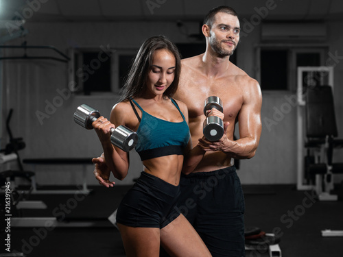 Male instructor and female train, lifting dumbbells