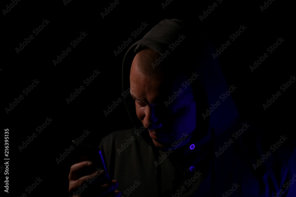 The man's portrait in a hood with the mobile phone in the dark. The man's portrait in a hood with the mobile phone in the dark.