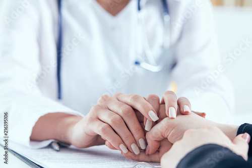 Friendly female doctor's hands holding female patient's hand for encouragement and empathy close-up. Partnership, trust and medical ethics concept.