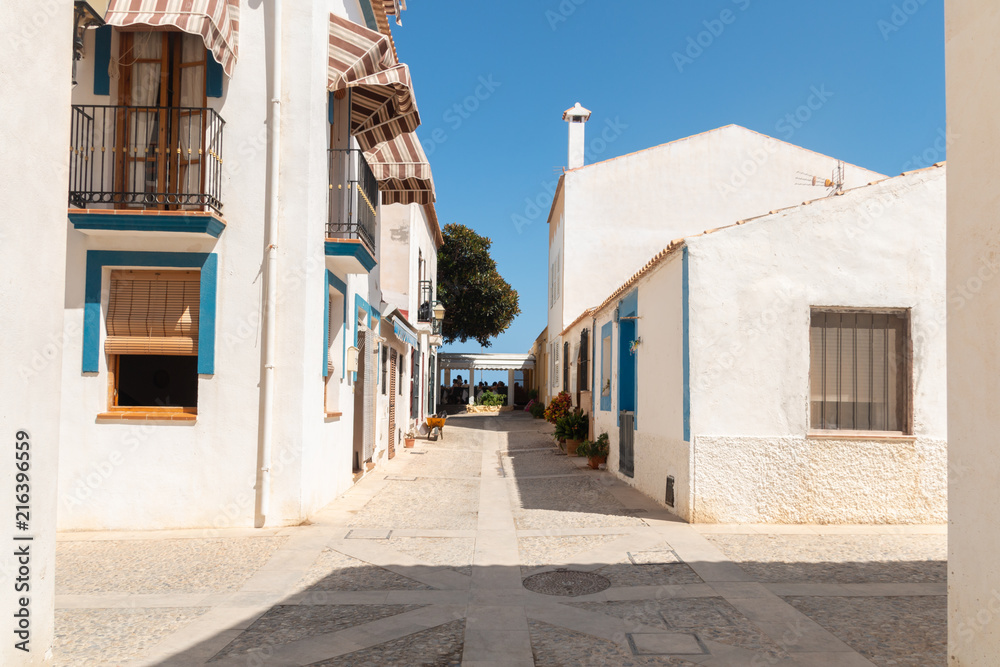 Narrow, stone street with bright, old houses on both sides. The buildings have nienieskie and colorful shutters in the windows. Tabarca, Spain, Europe. A beautiful, summer, sunny day.