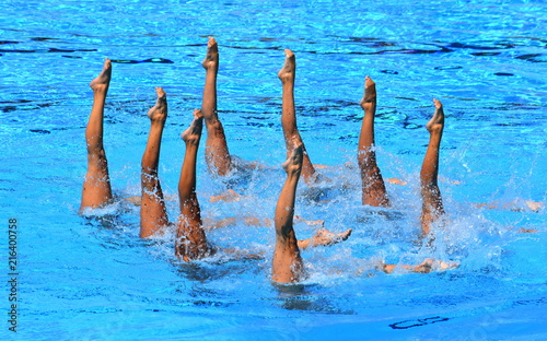 Synchronized Swimmers point up out of the water in action. Synchronized swimmers legs movement. Synchronized swimming team performing a synchronized routine of elaborate moves in the water.