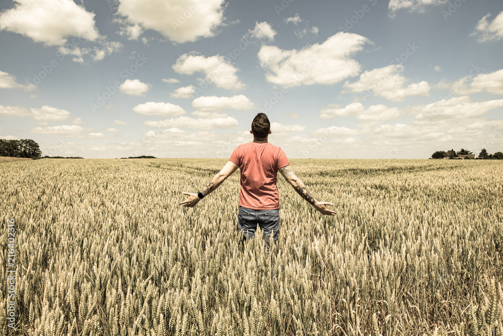 Young Man Standing in a Wheatfield with his Arms Stretched Out