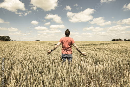 Young Man Standing in a Wheatfield with his Arms Stretched Out © peterotoole