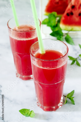 Cold watermelon lemonade with mint in a glass cup and slices of watermelon on a light background.