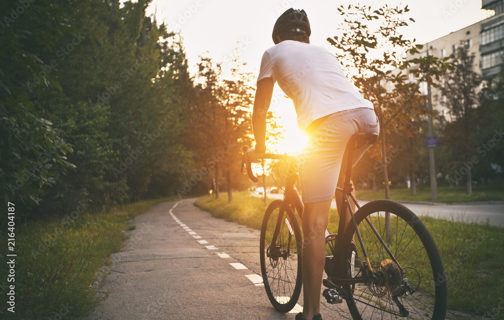 Fototapeta premium Młody chłopak w swobodnych ubraniach jeździ na rowerze po mieście wieczorem