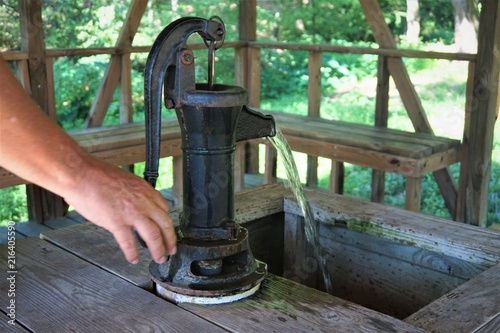 Old fashioned well pump is still working very well by manual it is in the wooden pavilion outdoor with the garden on the background , GA USA