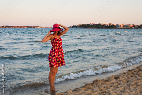 Young beautiful girl in red dress and in red hat at the sea.