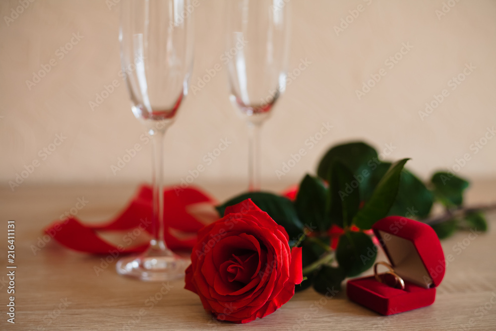 Two wineglasses, rings in red box and red rose are on the table for engagement. Two wineglasses, rings in red box and red rose are on the table for engagement.