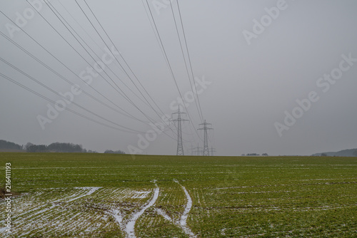 Power poles and lines at a field in winter with snowy tracks