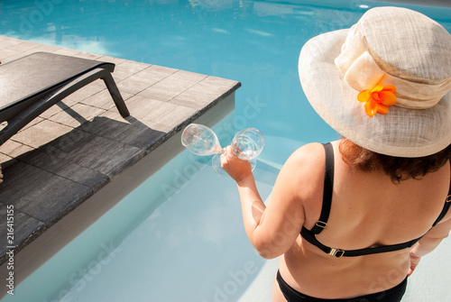 Milan, Italy - July 28, 2018: woman in a bathing suit, with a hat on her head, holds two glasses in her hands to toast in the pool
