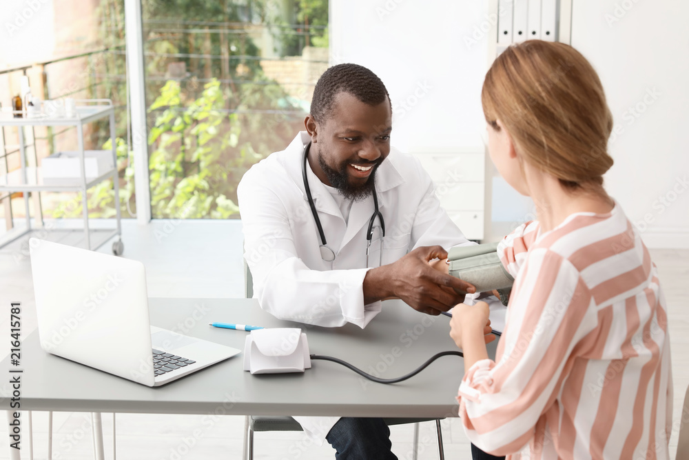Obraz premium Young African-American doctor checking patient's blood pressure in hospital