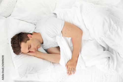 Young man sleeping on soft pillows in bed at home