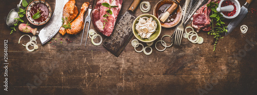 Various grill an bbq meats on rustic wooden background with aged kitchen and butcher tools, herbs, spices, seasoning and sauce, top view, border