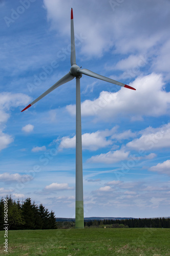 Windkraftanlage auf einer Wiese vor blauen Himmel mit weißen Wolken
