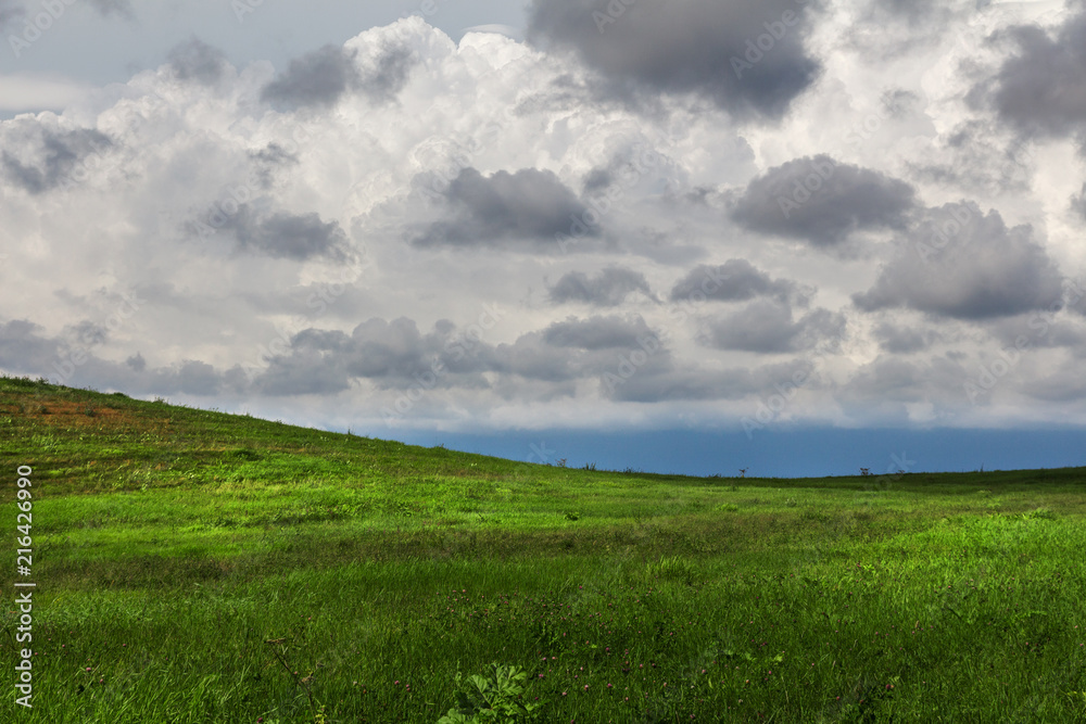 green hilly field and gloomy cloudy sky