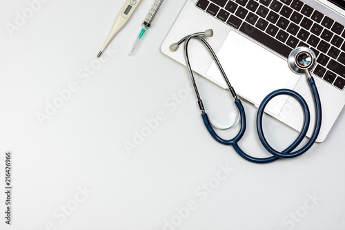 Stethoscope on laptop computer with syringe and thermometer at doctor workplace table  top view design
