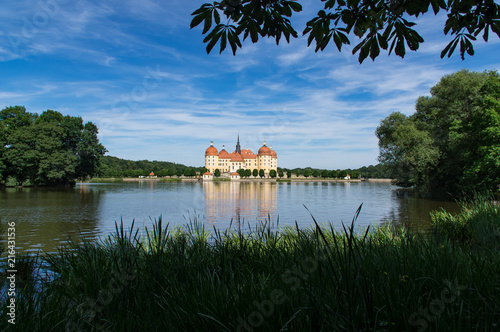 Schloß Moritzburg umrahmt von grüner Natur vor blauen Himmel