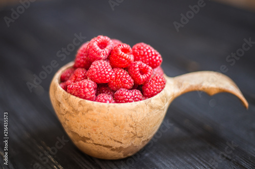 Wooden bowl with raspberries on black table. Macro