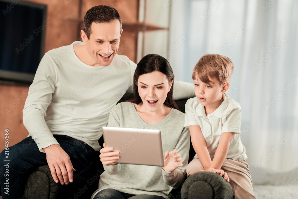 So interesting. Pleasant young woman holding a tablet while sitting together with her family So interesting. Pleasant young woman holding a tablet while sitting together with her family