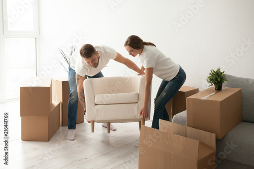 Quadro em tela Young couple carry chair to new living room after moving in to shared apartment,