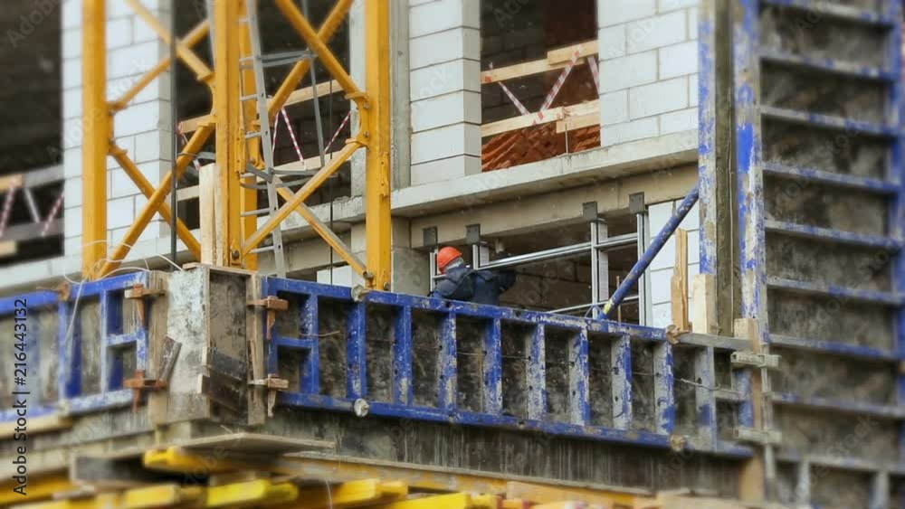 Work puts windows in snowy weather. A worker in a helmet at the height works on a construction site. Work puts windows in snowy weather. A worker in a helmet at the height works on a construction site.